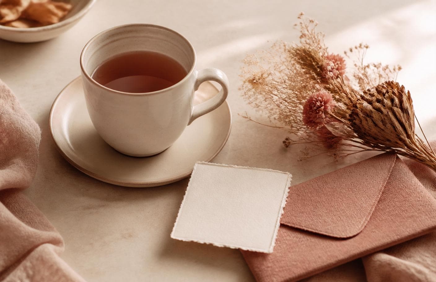 A warm cup of tea, a handwritten note, and dried flowers on a cream table